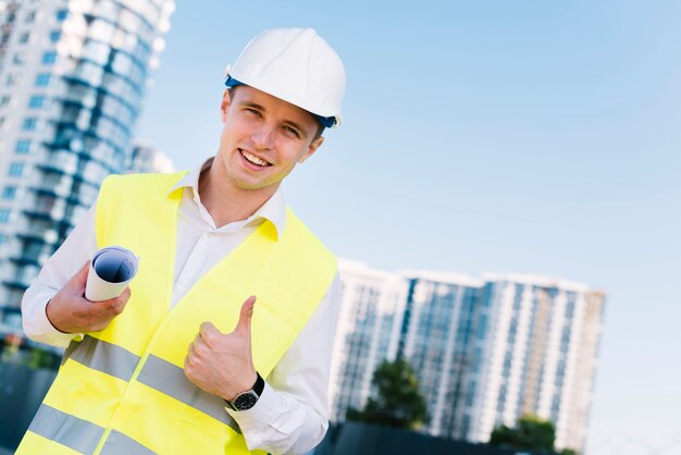 Joven arquitecto de ángulo bajo con planos y casco