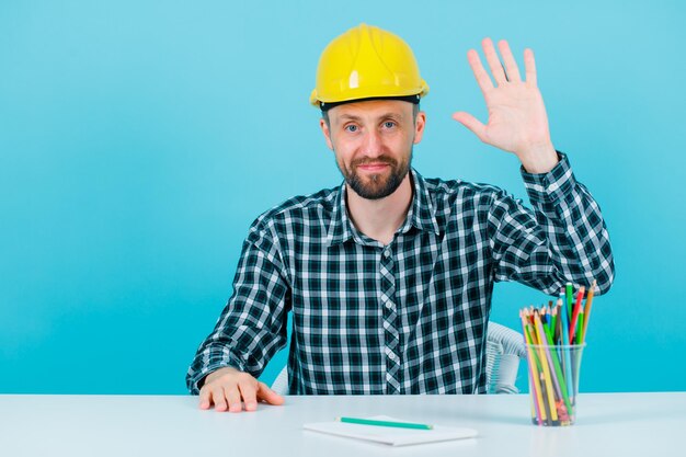 El joven arquitecto se está levantando y mostrando su puñado sobre fondo azul.