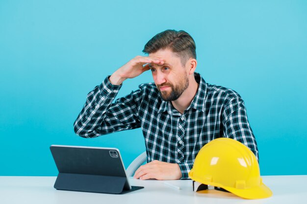 El joven arquitecto está mirando hacia otro lado sosteniendo un puñado detrás de la frente sobre fondo azul.