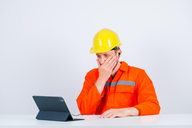 El joven arquitecto está mirando su tableta con la mano en la boca sobre fondo blanco.