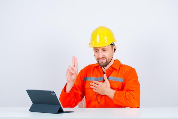 El joven arquitecto muestra dos gestos y pone la otra mano en la cintura sentándose frente a la tableta en el fondo blanco