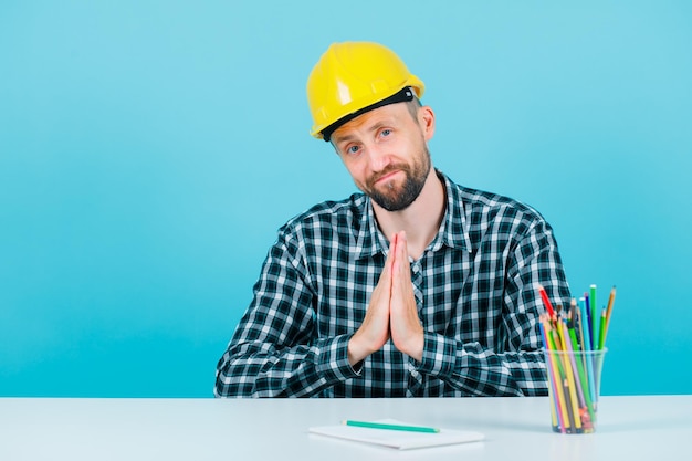 El joven arquitecto muestra un gesto de mendicidad tomándose de la mano en el fondo azul