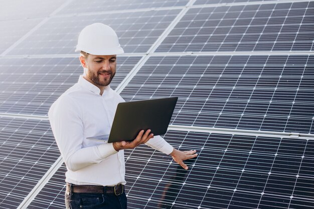 Joven arquitecto de pie junto a paneles solares haciendo diagnósticos en computadora