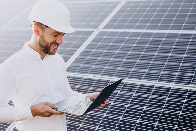 Joven arquitecto de pie junto a paneles solares haciendo diagnósticos en computadora