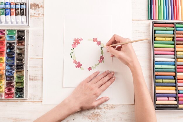 Joven artista dibujo patrón de flores con pintura de acuarela y pincel en el lugar de trabajo