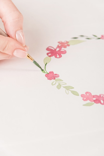 Joven artista dibujo patrón de flores con pintura de acuarela y pincel sobre papel en el lugar de trabajo