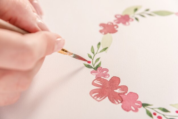 Joven artista dibujo patrón de flores con pintura de acuarela y pincel sobre papel en el lugar de trabajo