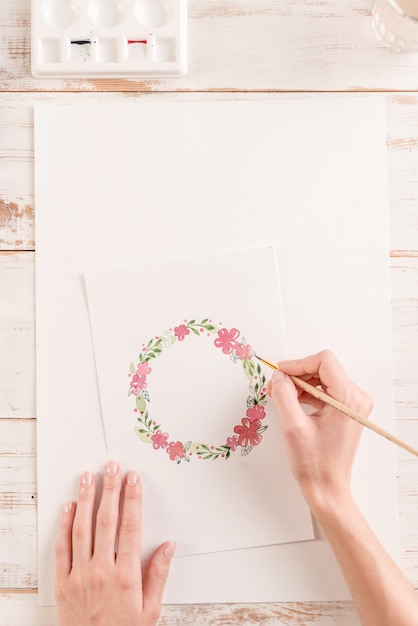 Joven artista dibujo patrón de flores con pintura de acuarela y pincel sobre papel en el lugar de trabajo