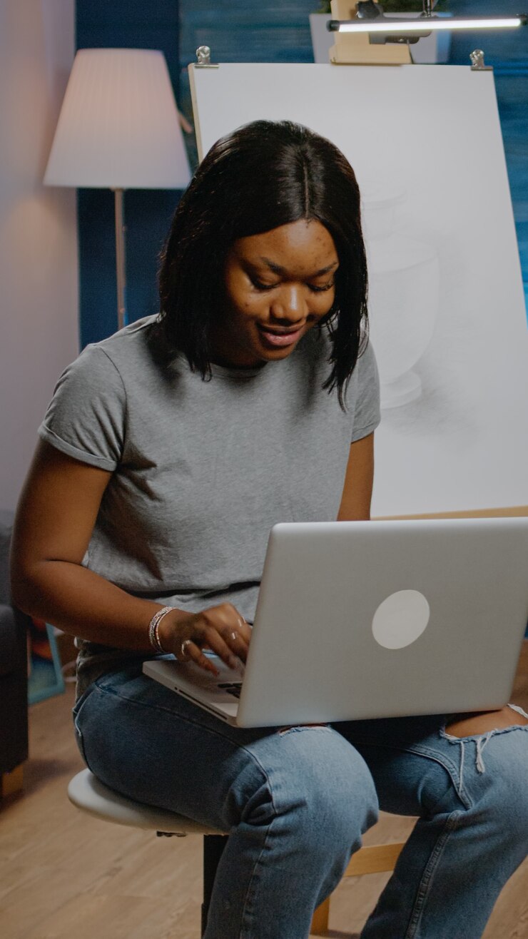 Foto gratuito joven artista de etnia afroamericana que usa computadora portátil en busca de inspiración para la técnica de dibujo en la sala de creatividad. mujer negra con tecnología moderna trabajando en una obra maestra