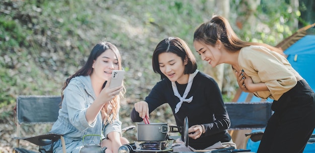 Una joven asiática cocinando y su amiga disfrutan de hacer la comida en una olla. Hablan y se ríen juntos mientras acampan en el parque natural.