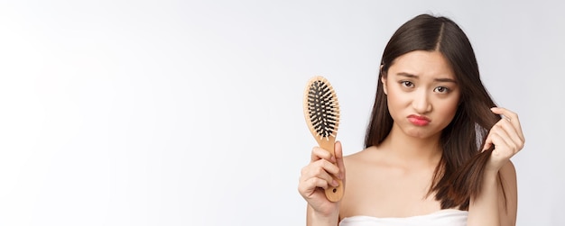 Una joven asiática estresada y molesta sosteniendo el cabello seco dañado en las manos sobre un fondo blanco aislado