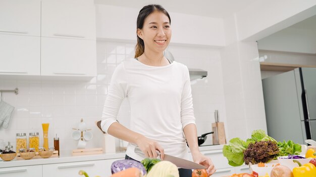 Joven asiática haciendo ensalada de comida sana en la cocina