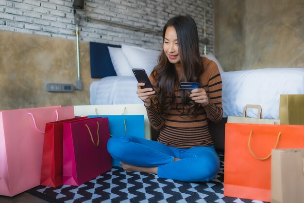 Joven asiática con teléfono móvil inteligente y computadora portátil con tarjeta de crédito para comprar en línea