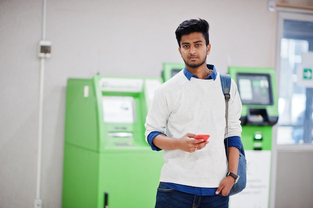 Foto gratuita joven asiático con estilo con teléfono móvil y mochila contra la fila de cajero automático verde