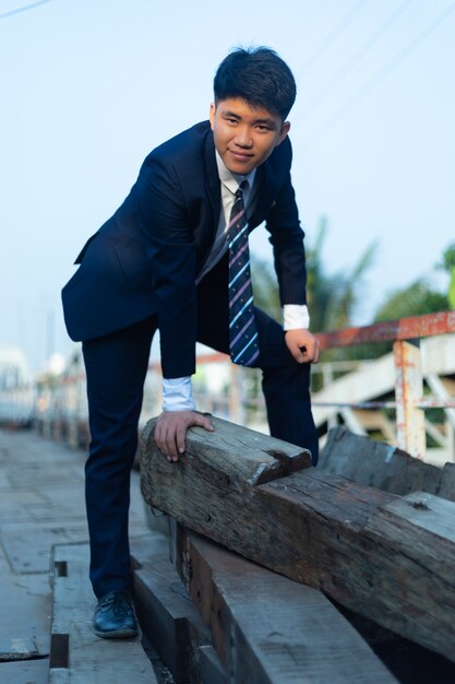 Joven asiático en un traje agachado sobre un montón de troncos