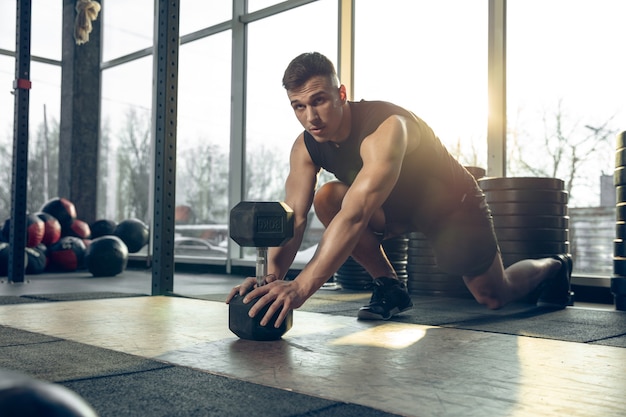 Joven atleta caucásico muscular entrenando en el gimnasio, haciendo ejercicios de fuerza, practicando, trabajando en la parte superior del cuerpo con pesas rodando.