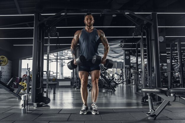 Joven atleta caucásico muscular practicando en el gimnasio con las pesas.