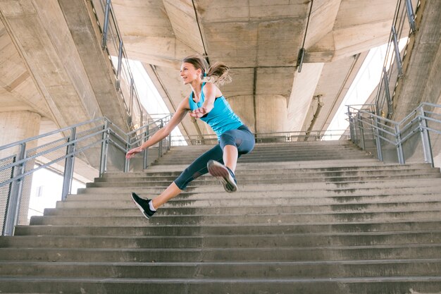 Joven atleta femenina en ropa deportiva saltando por encima de la escalera de hormigón