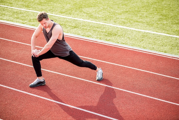 Joven atleta masculino estirando su cuerpo en la pista de carreras