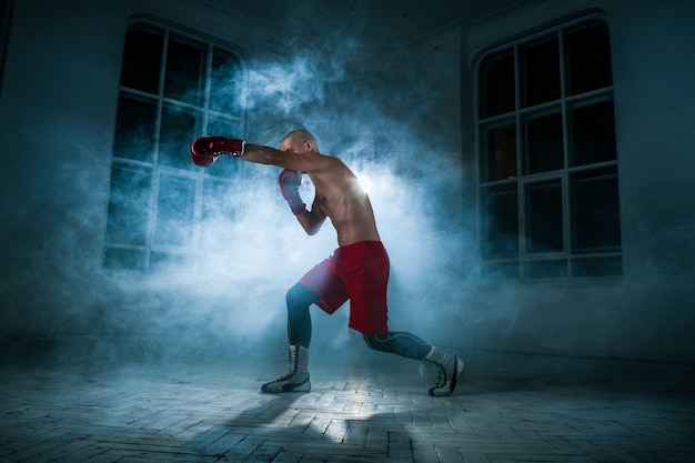 El joven atleta masculino kickboxing en un humo azul