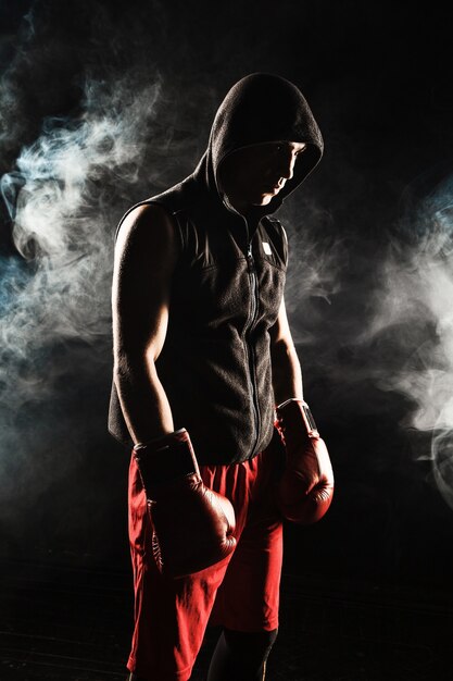 El joven atleta masculino kickboxing de pie sobre un fondo de humo azul