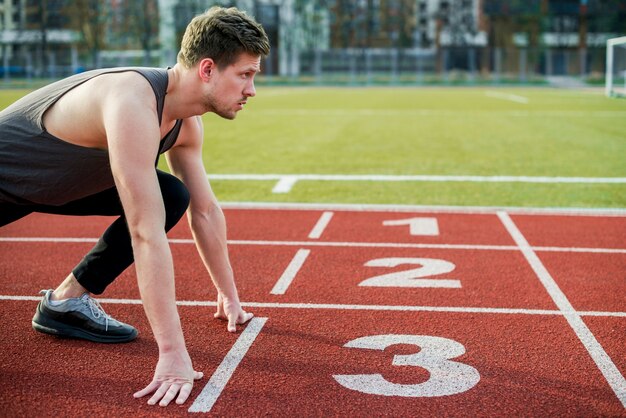 Joven atleta masculino listo para correr tomando posición en la línea de salida