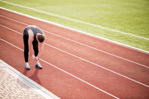 Joven atleta masculino de pie en la pista de carreras estirando sus manos