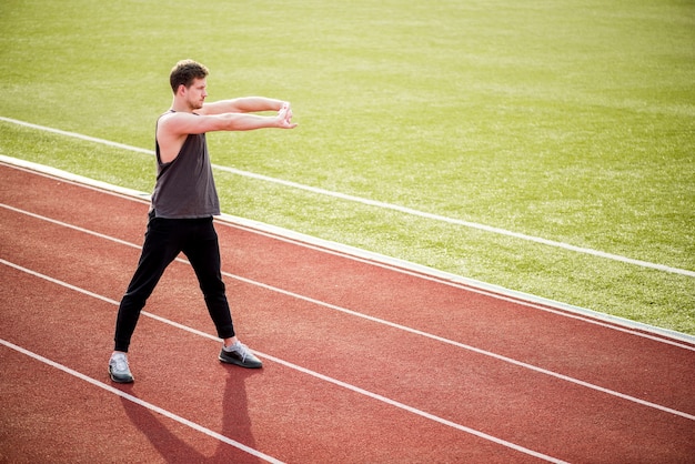 Joven atleta masculino de pie en la pista de carreras estirando sus manos