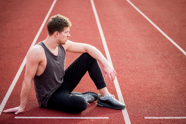 Joven atleta masculino sentado en la línea de inicio de la pista