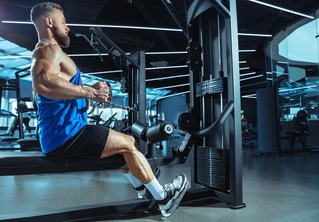 Joven atleta muscular entrenando en el gimnasio, haciendo ejercicios de fuerza, practicando