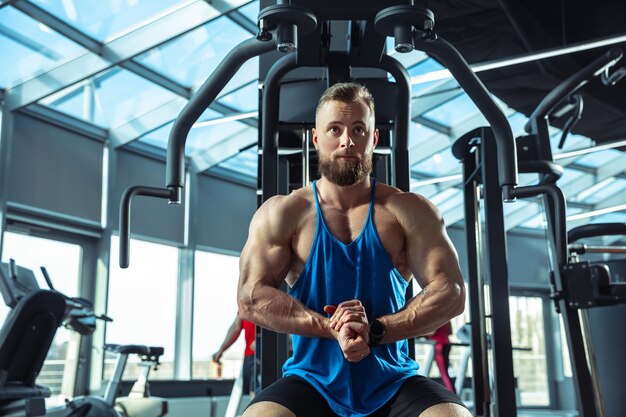 Joven atleta muscular entrenando en el gimnasio, haciendo ejercicios de fuerza, practicando