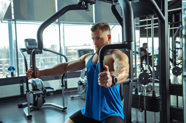 Joven atleta muscular entrenando en el gimnasio, haciendo ejercicios de fuerza, practicando