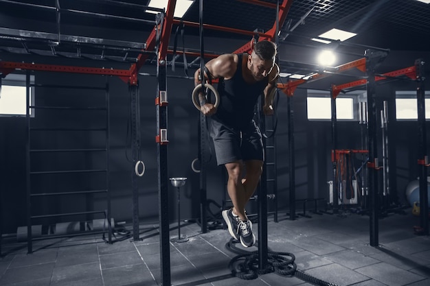 Joven atleta muscular practicando dominadas en el gimnasio con los anillos