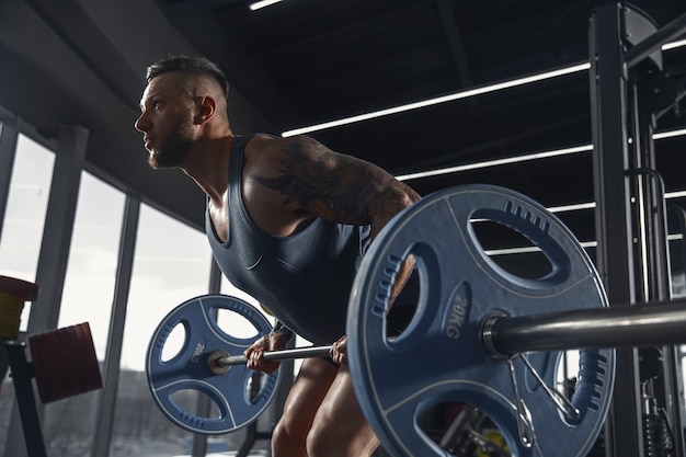 Joven atleta muscular practicando dominadas en el gimnasio con barra