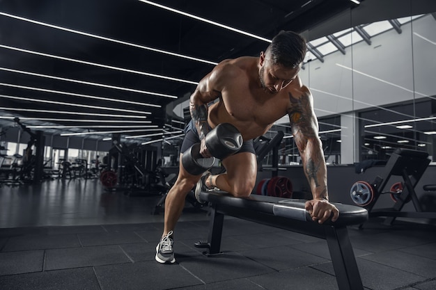 Joven atleta musculoso practicando en el gimnasio con las pesas