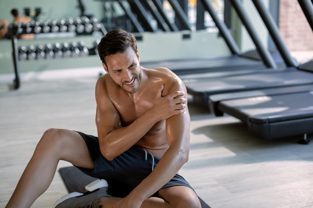 Joven atleta sosteniendo su hombro con dolor después del entrenamiento deportivo en un gimnasio