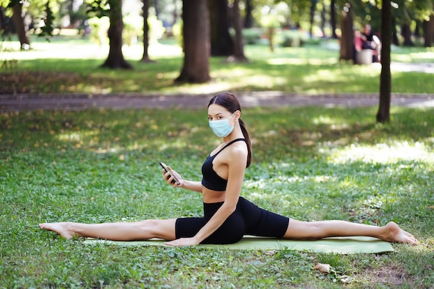 Joven atlética en una máscara protectora médica, haciendo yoga en el parque