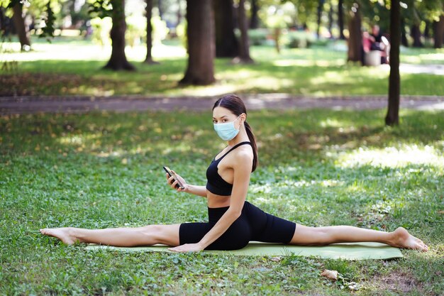 Joven atlética en una máscara protectora médica, haciendo yoga en el parque