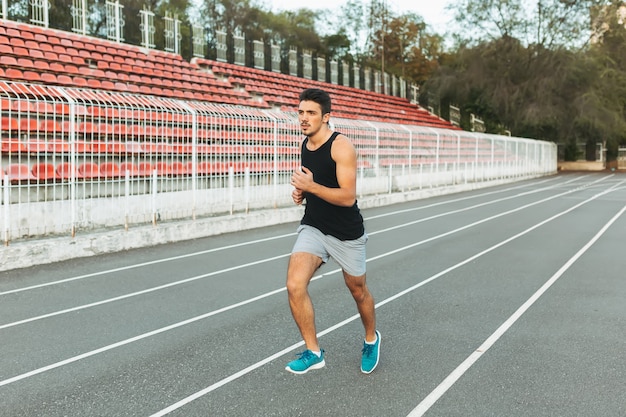 Joven atlético corriendo en el estadio en la mañana