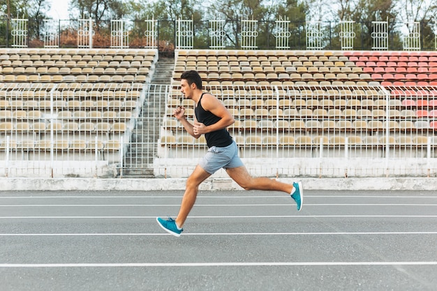 Joven atlético corriendo en el estadio en la mañana