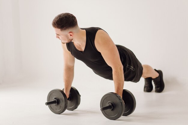 Joven atlético haciendo entrenamientos en casa, hombre haciendo entrenamiento, calentamiento antes del ejercicio con pesas.