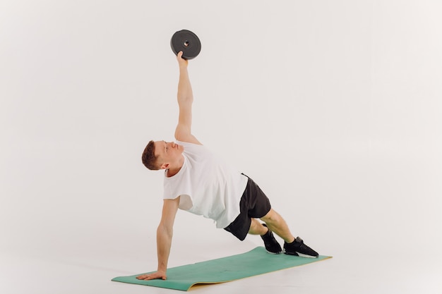 Joven atlético haciendo entrenamientos en casa, hombre haciendo entrenamiento, calentamiento antes del ejercicio con pesas.