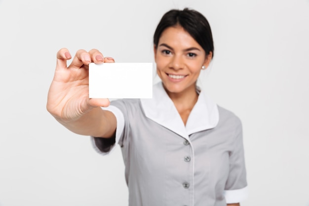 Joven y atractiva ama de casa femenina en uniforme mostrando corte vacío, enfoque selectivo en tarjeta