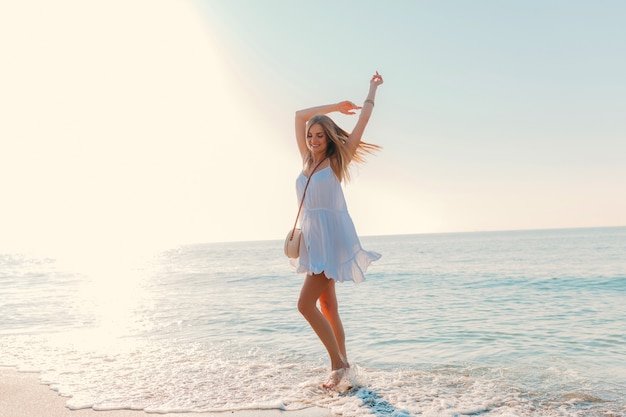 Joven atractiva mujer feliz bailando dando la vuelta por el estilo de moda de verano soleado de playa de mar en vacaciones de vestido blanco