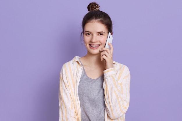 Joven y atractiva mujer joven de pelo oscuro con teléfono móvil conversando con un amigo