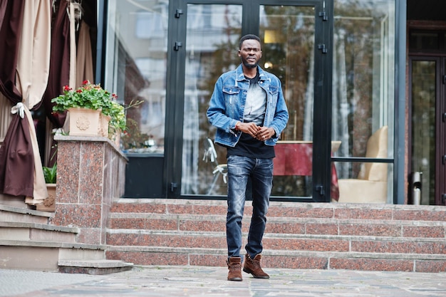 Joven atractivo hombre afroamericano serio modelo moderno chico guapo en chaqueta de jeans de pie en la calle de la ciudad urbana