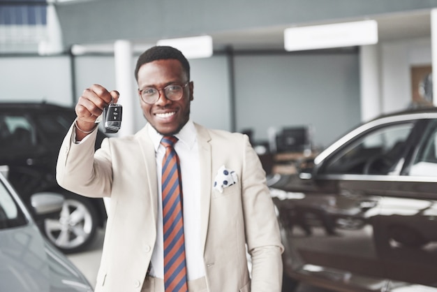 El joven y atractivo hombre de negocios negro compra un coche nuevo, tiene las llaves en la mano. Los sueños se hacen realidad