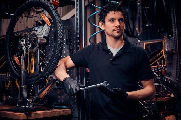 Un joven y atractivo mecánico posa junto a una bicicleta en su propio taller.