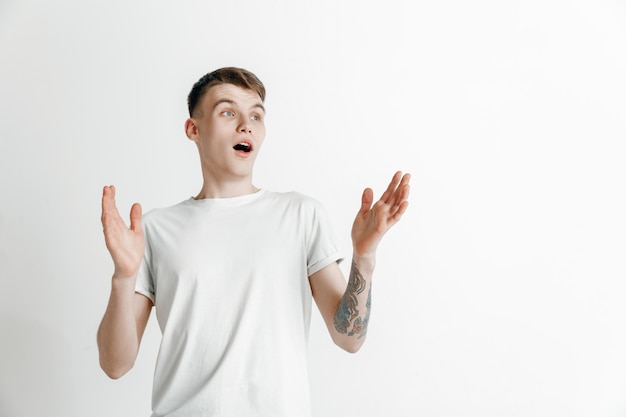 El joven atractivo mirando sorprendido aislado en gris