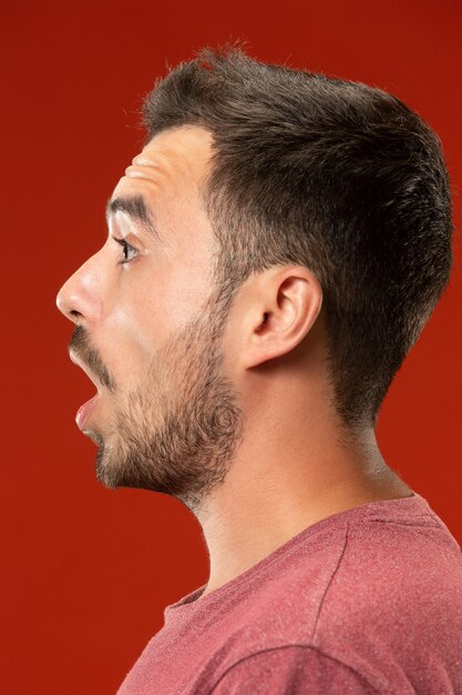 El joven atractivo mirando sorprendido aislado en rojo